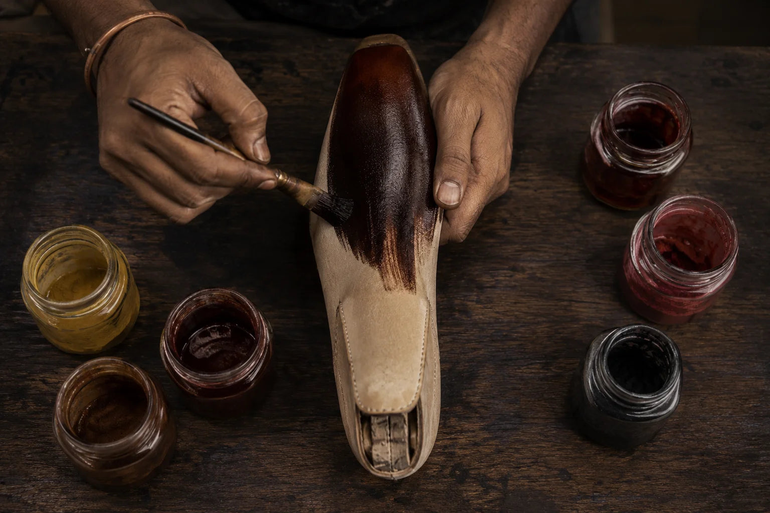 Craftsman hand-applying patina to a leather shoe with a brush